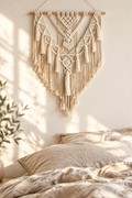 Tapiz de macramé color crema sobre una cama de lino con luz de mañana